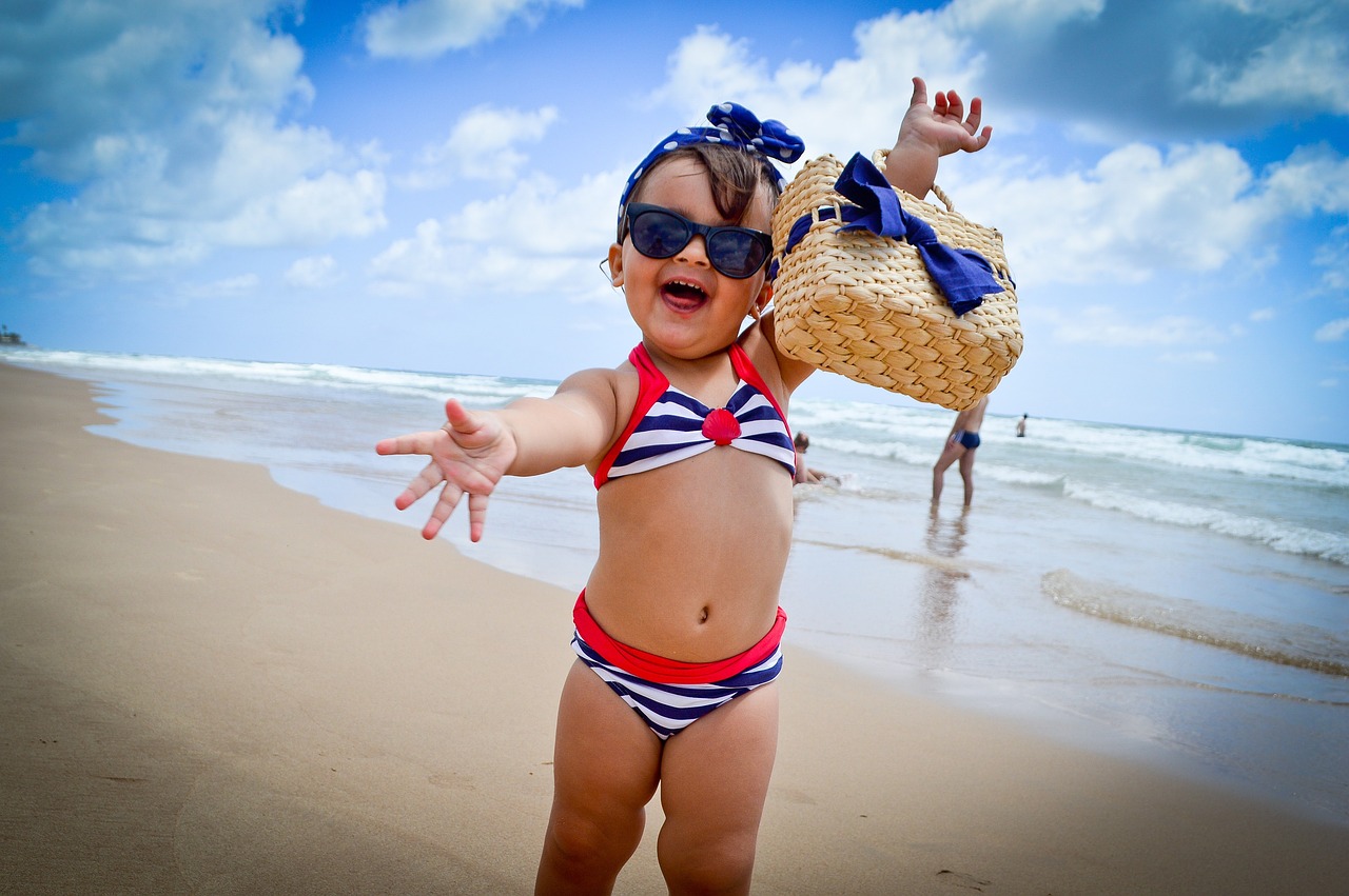 Babymädchen am Strand / Meer mit Sonnenbrille und Handtasche